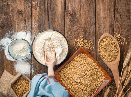 Flour in a bowl, wheat and spikelets on a wooden background. Top view, horizontal.