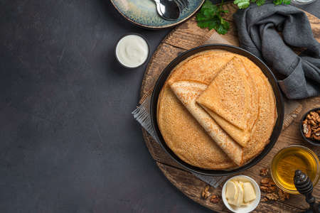 Fried pancakes on a dark background with honey, sour cream and nuts. Pancake day. Top view, copy...