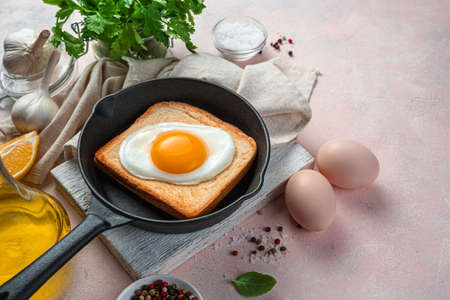 Fried egg on toast in a frying pan on a light background with spices and fresh herbs. Side view,...