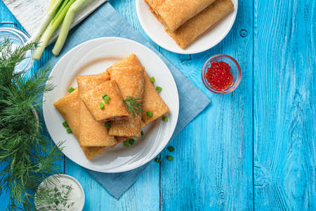 Stuffed pancakes with red caviar, sour cream and fresh herbs on a blue background. Traditional Russian pancakes. Top view, copy space.の写真素材