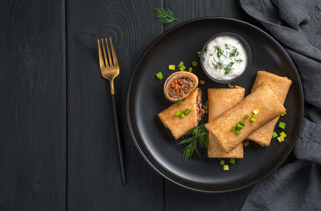 Stuffed pancakes with meat and carrots on a black background. Top view, copy space.