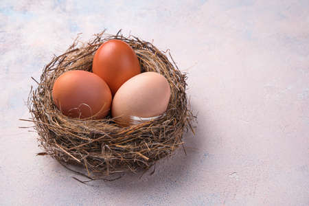 Three chicken eggs in a nest on a light background. Side view, copy space.