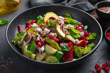 Vegetable salad with avocado, beetroot, cucumber and feta cheese seasoned with pomegranate, sesame and flax seeds and nuts. Side view, close up. Cleansing salad is rich in antioxidants.の写真素材