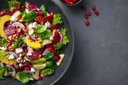 Salad with beetroot and avocado, fresh herbs, feta cheese, nuts and seeds on a gray-brown background. Top view, copy space.の写真素材