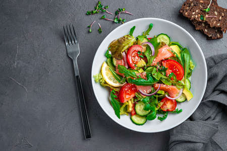 Salad with salmon, avocado, cucumber and tomatoes on a graphite background. Top view, copy space.の写真素材