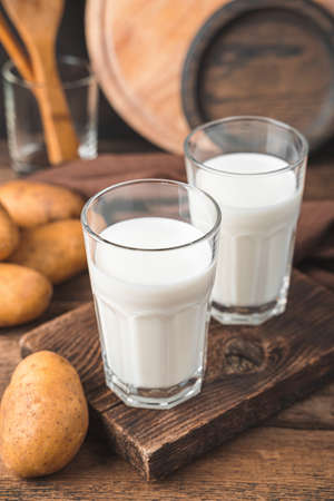 Two glasses of potato milk with raw potatoes on a brown background. Vegetarian milk. side view, vertical.の写真素材
