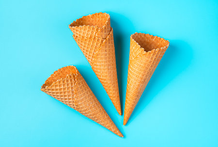 Crispy empty ice cream cones on a light blue background. Top view, horizontal
