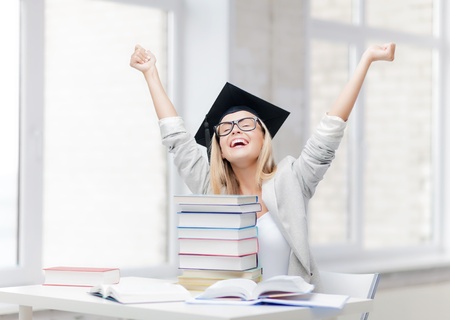 happy student in graduation cap with stack of booksの写真素材