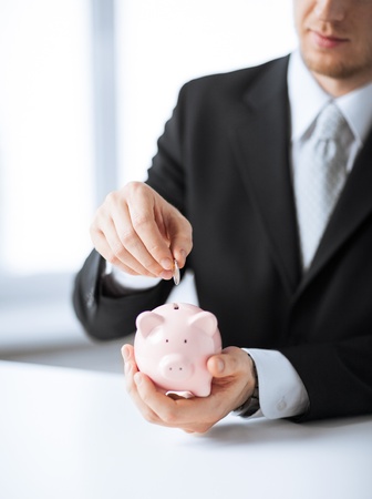 picture of man putting coin into small piggy bankの写真素材