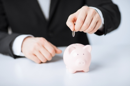 picture of man putting coin into small piggy bankの写真素材