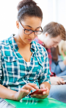 education concept - smiling international student girl with smartphone at schoolの写真素材