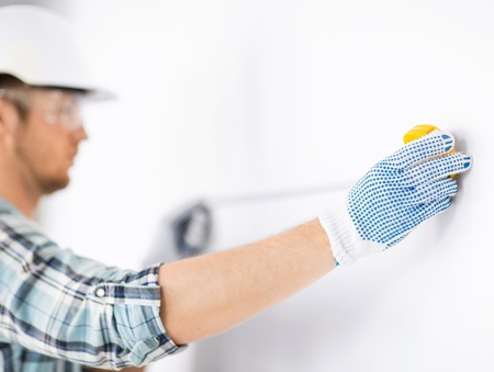 architecture and home renovation concept - male architect measuring wall with flexible ruler