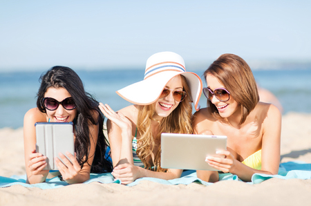 summer holidays, technology and internet concept - girls in bikinis with tablet pc sunbathing on the beachの写真素材