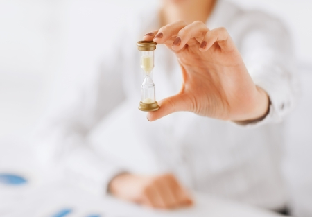 business, time management, deadline concept - woman hand with sandglassの写真素材