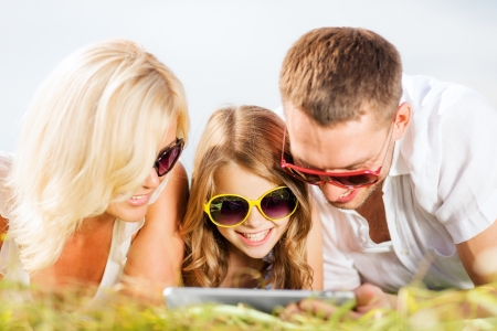 summer holidays, children and people concept - happy family with tablet pc, blue sky and green grass taking pictureの写真素材