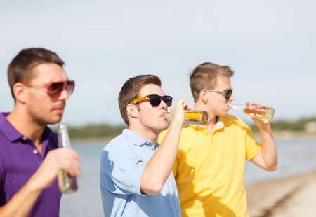 summer, holidays, vacation, happy people concept - group of friends having fun on the beach with bottles of beer or non-alcoholic drinksの写真素材
