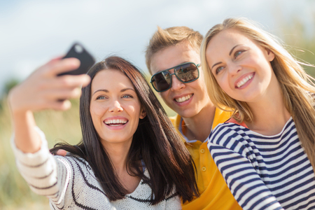 summer, holidays, vacation, happy people concept - group of friends taking photo picture with smartphoneの写真素材