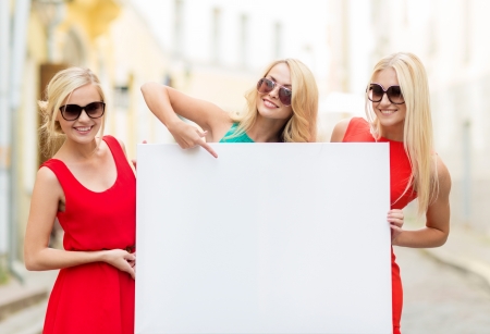 summer holidays, , travel, tourism and advertisement concept - three happy blonde women with blank white board in the cityの写真素材