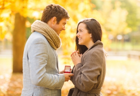 holidays, love, couple, relationship and dating concept - romantic man proposing to a woman in the autumn parkの写真素材