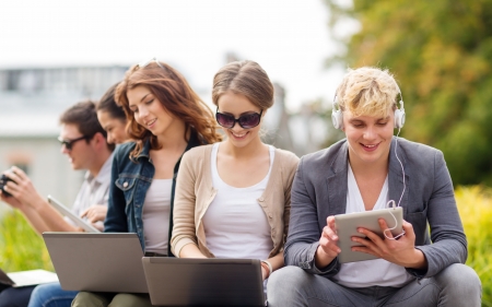 summer, internet, education, campus and teenage concept - group of students or teenagers with laptop and tablet computers hanging outの写真素材