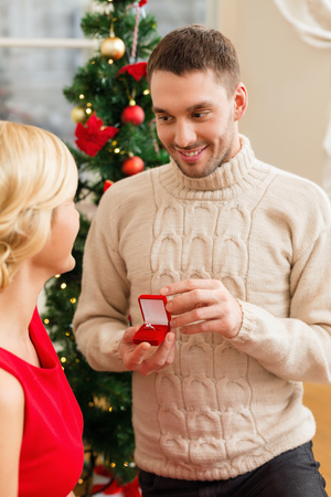 love, couple, christmas, x-mas, winter, relationship and dating concept - romantic man proposing to a woman in red dressの写真素材