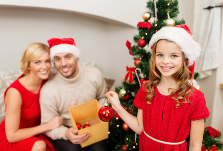 family, christmas, x-mas, winter, happiness and people concept - smiling family in santa helper hats decorating christmas treeの写真素材