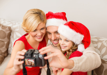 family, christmas, x-mas, winter, happiness and people concept - smiling family in santa helper hats taking picture with photo cameraの写真素材
