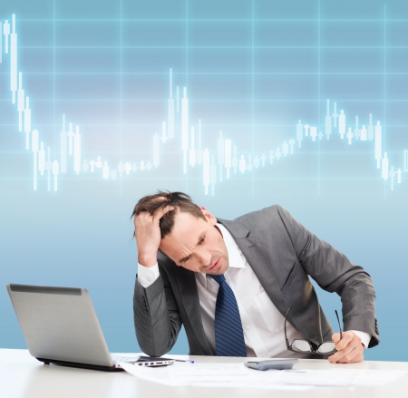 business, office and money concept - stressed businessman in black eyelgasses with laptop computer, papers, calculator and forex chartの写真素材