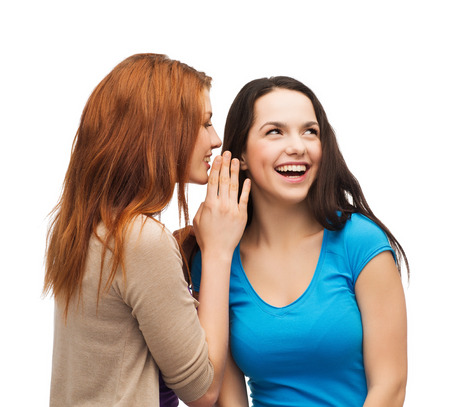 friendship, happiness and people concept - two smiling girls whispering gossipの写真素材
