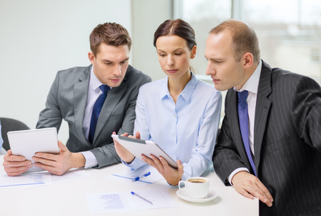 business, technology and office concept - serious business team with tablet pc computer, documents and coffee having discussion in officeの写真素材