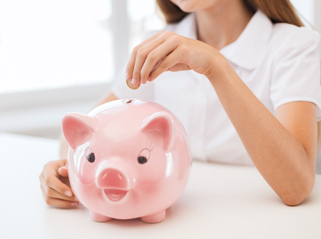 education, school and money saving concept - smiling child putting coin into big piggy bankの写真素材
