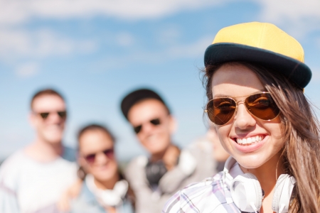 summer holidays and teenage concept - teenage girl in sunglasses, cap and headphones hanging out with friends outsideの写真素材