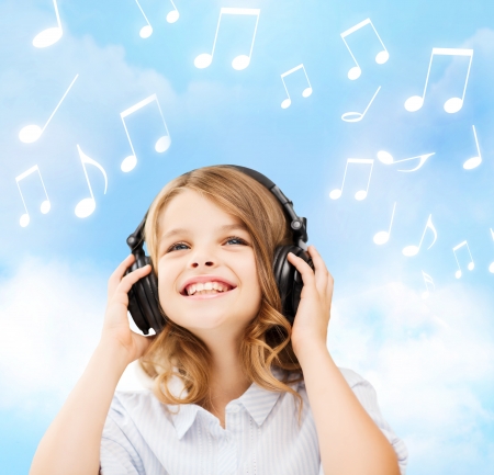 home, leisure, new technology and music concept - smiling little girl with headphones over blue sky background and music notesの写真素材