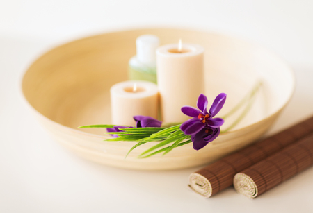 spa, health and beauty concept - candles and iris flowers in wooden bowl and bamboo matの写真素材
