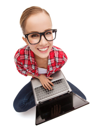 education, technology and internet concept - smiling teenage girl in black eyeglasses with laptop computerの写真素材