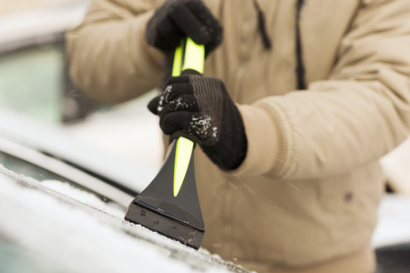 transportation, winter and vehicle concept - closeup of man scraping ice from car windshield with brushの写真素材