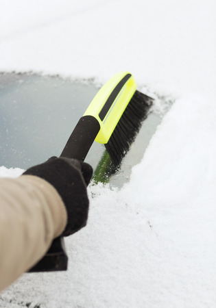 transportation, winter and vehicle concept - closeup of man cleaning snow from car windshield with brushの写真素材