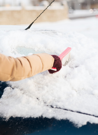 transportation, winter and vehicle concept - closeup woman cleaning snow from car back window with brushの写真素材