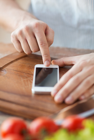 cooking, technology and home concept - closeup of man pointing finger to smartphoneの写真素材