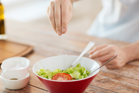 cooking and home concept - close up of male hands flavouring salad in a bowl with saltの写真素材