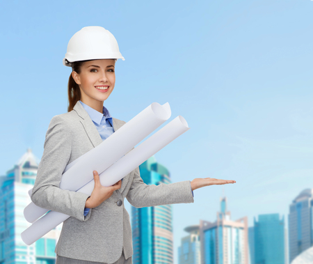 building, developing, consrtuction and architecture concept - smiling architect in helmet with blueprints showing something on palm of handの写真素材