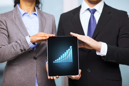 business, technology, internet and office concept - businessman and businesswoman with graph on tablet pc screen in officeの写真素材
