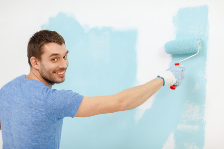 repair, building and home concept - smiling man painting wall at homeの写真素材