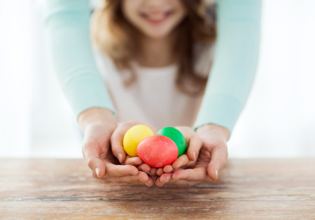 easter, family, holiday and child concept - close up of little girl and mother holding colored eggsの写真素材