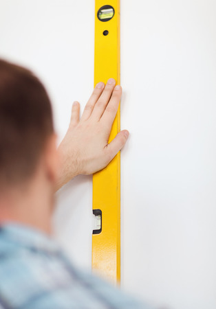 repair, building, technology and home concept - close up of male with spirit level mesuring wallの写真素材