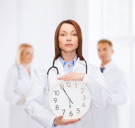 healthcare and medicine concept - calm female doctor with wall clock and stethoscopeの写真素材