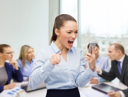 business, technology and education concept - screaming businesswoman with smartphone in officeの写真素材