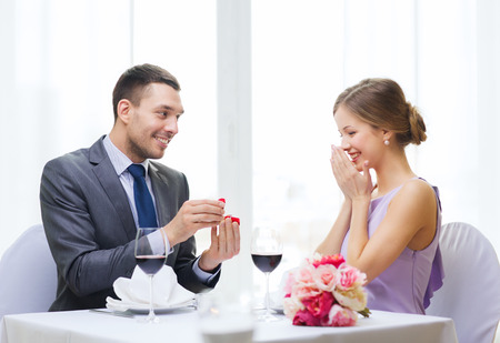 restaurant, couple and holiday concept - smiling man proposing to his girlfriend at restaurantの写真素材