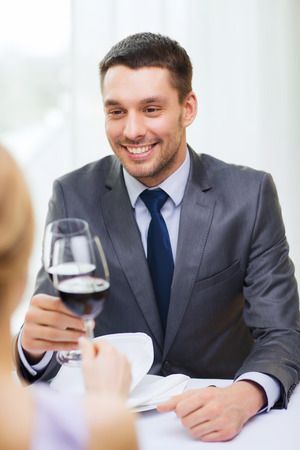 restaurant, couple and holiday concept - smiling young man with glass of red wine looking at girlfriend or wife at restaurantの写真素材