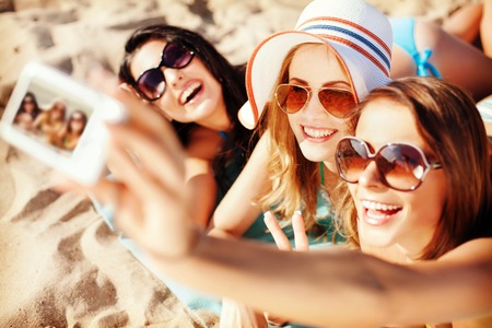 summer holidays, technology and beach concept - girls making self portrait on the beachの写真素材